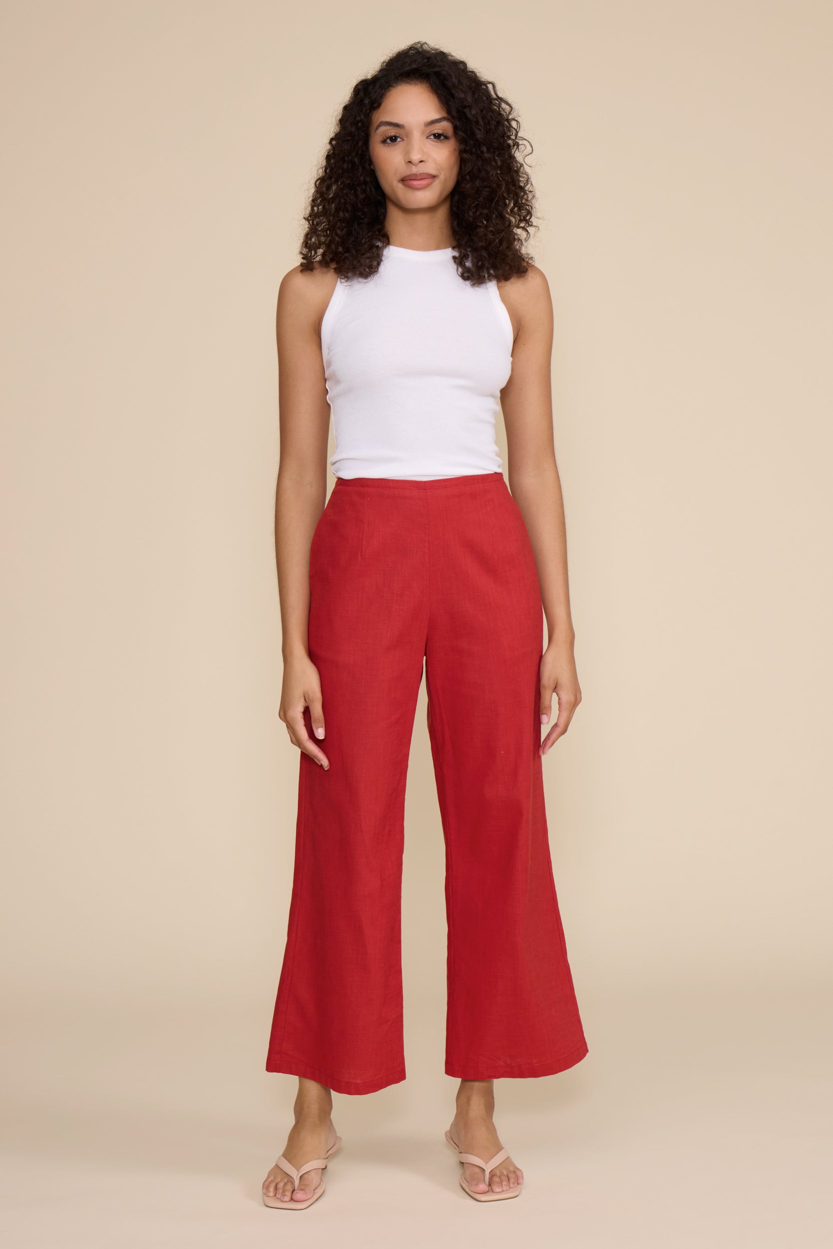 A woman modeling a white sleeveless top and bright red wide-leg cropped pants against a solid beige studio background.