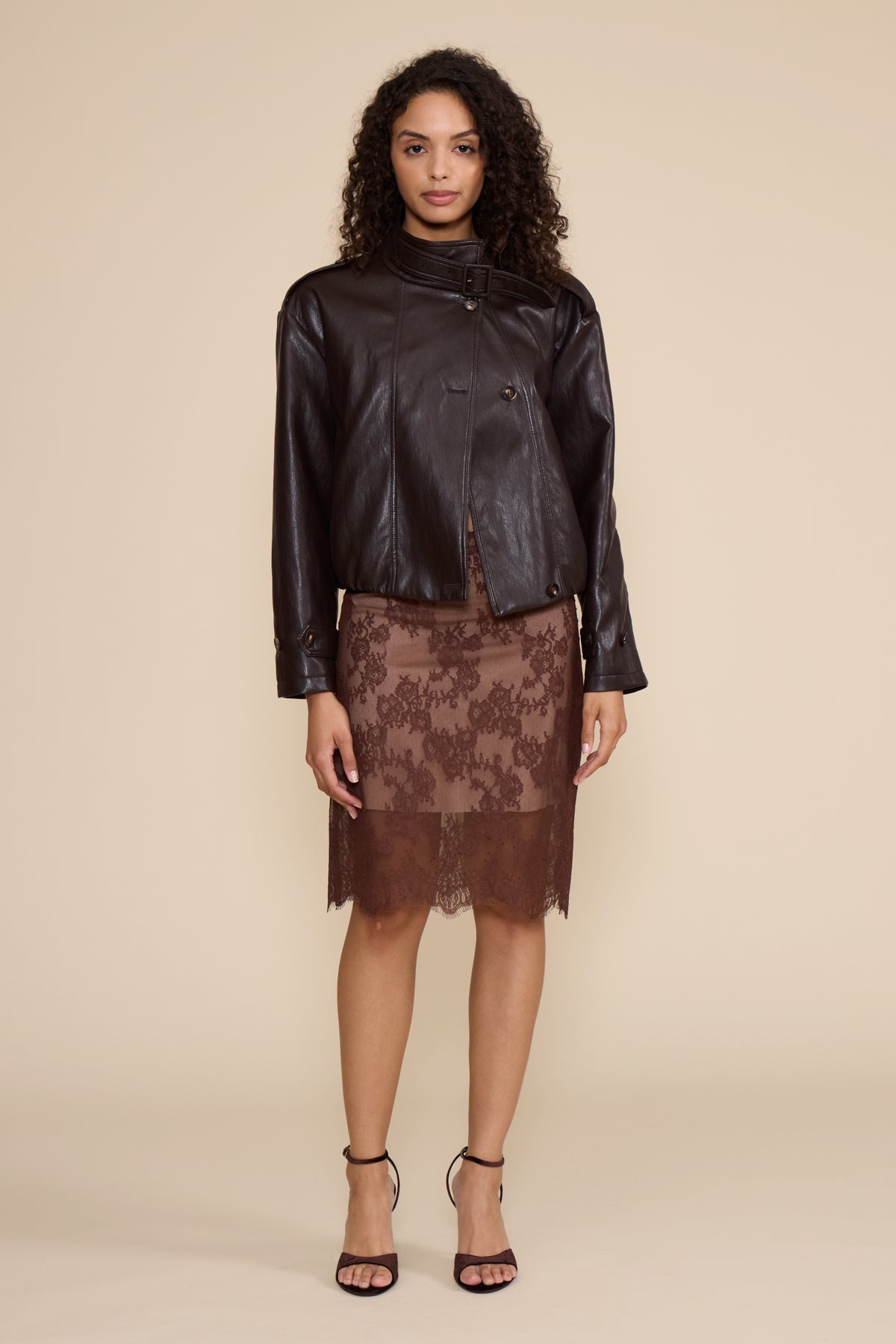 Woman wearing a black leather jacket and brown lace skirt on a beige background