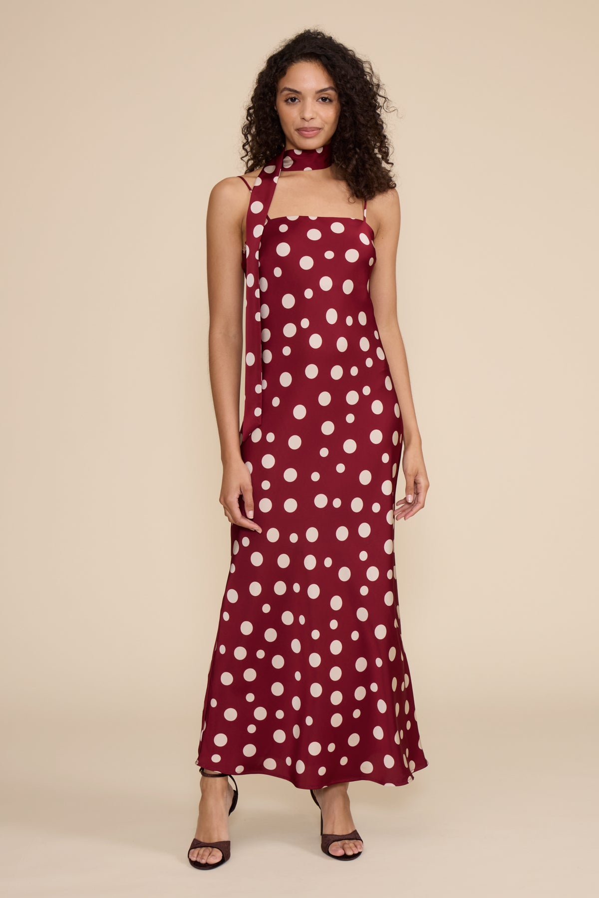 Woman wearing a burgundy dress with white polka dots against a beige background