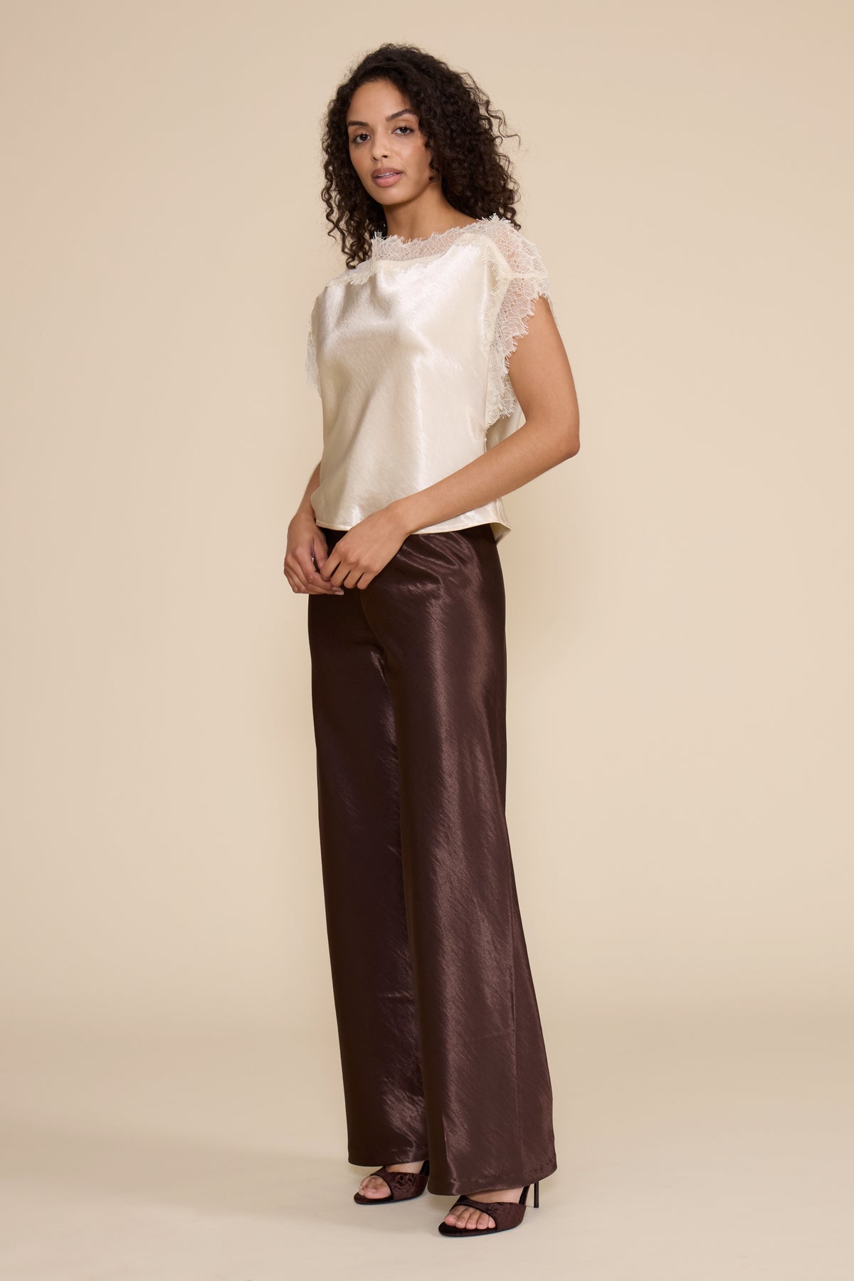 Woman wearing a white top and brown pants on a beige background