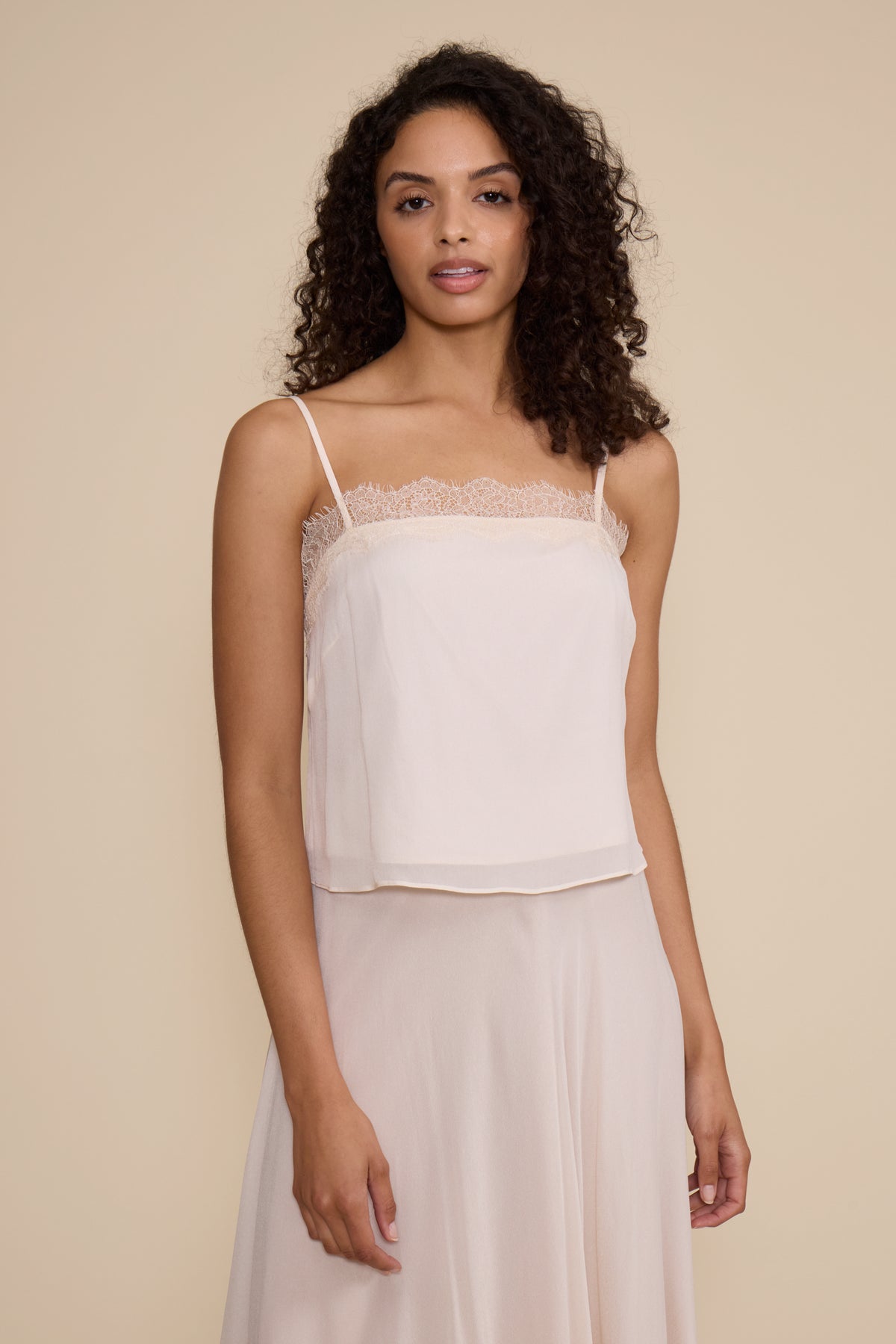Woman wearing a white lace-trimmed top and skirt against a beige background