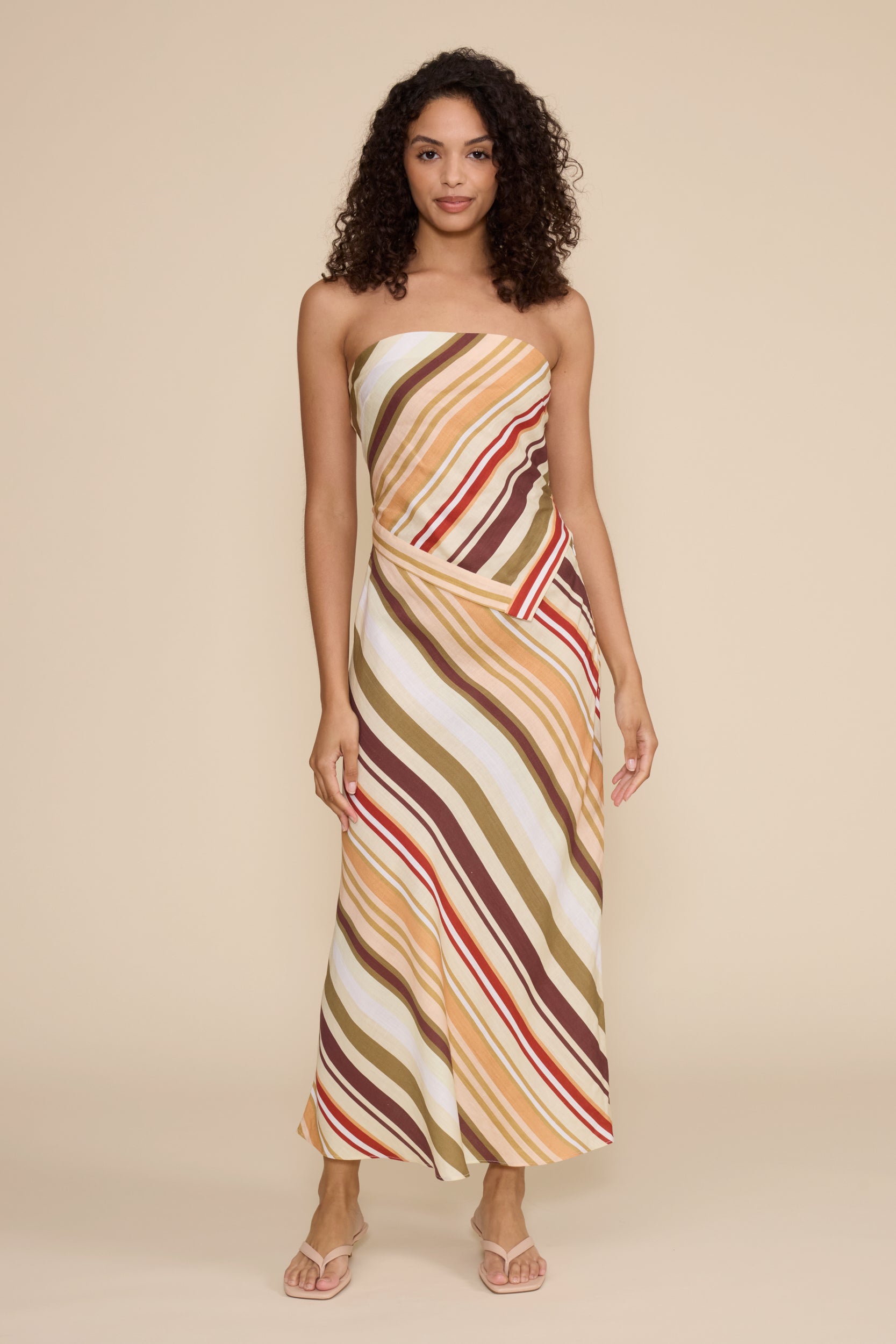 Woman wearing a strapless, long, multicolored striped dress against a beige background