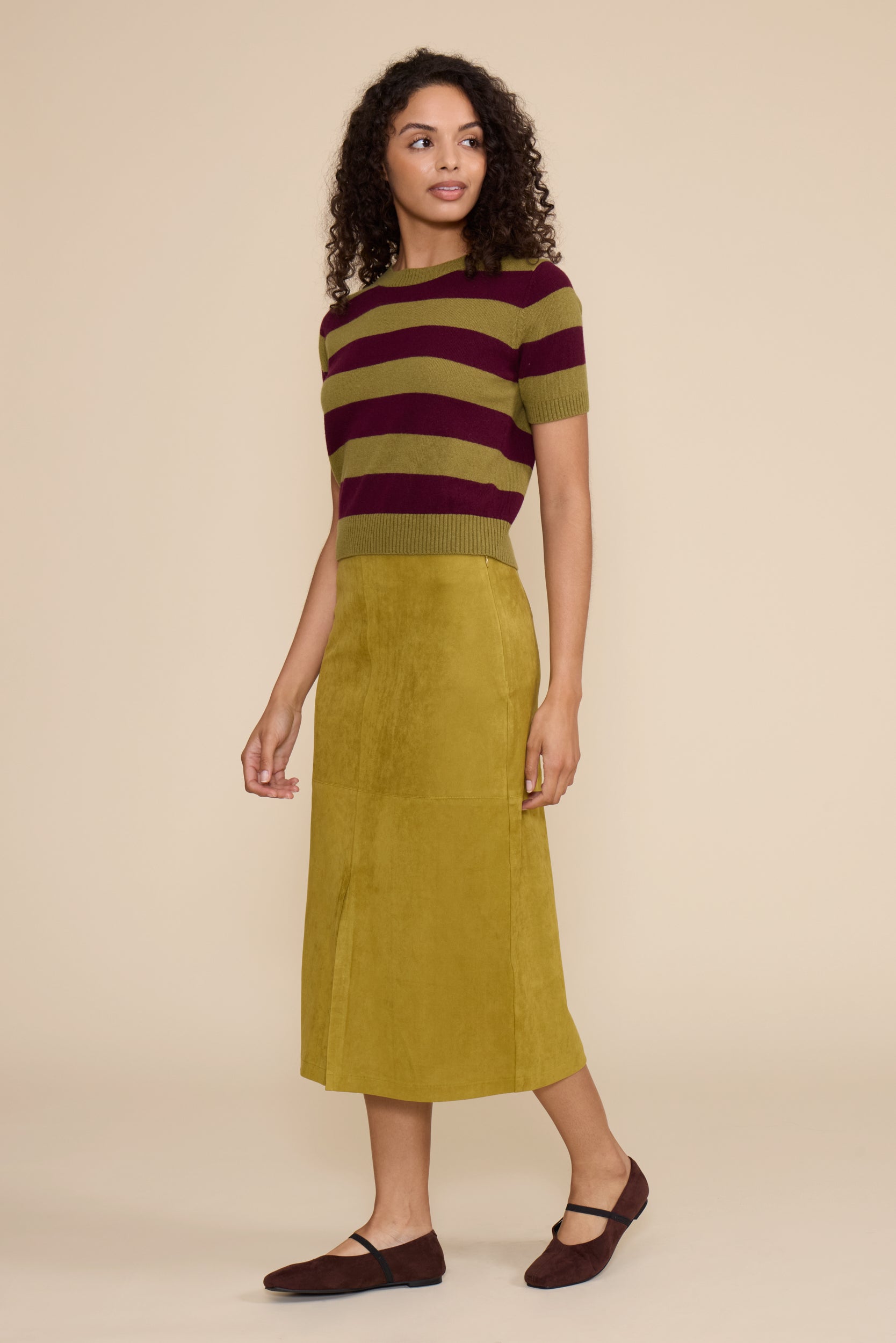 Woman wearing a striped sweater and green skirt on a beige background