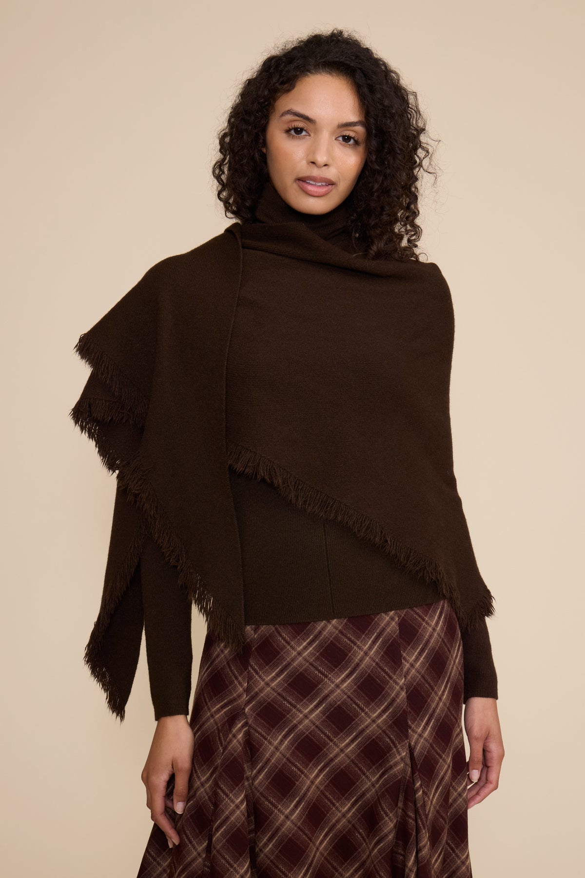 Woman wearing a black poncho over a plaid skirt on a beige background