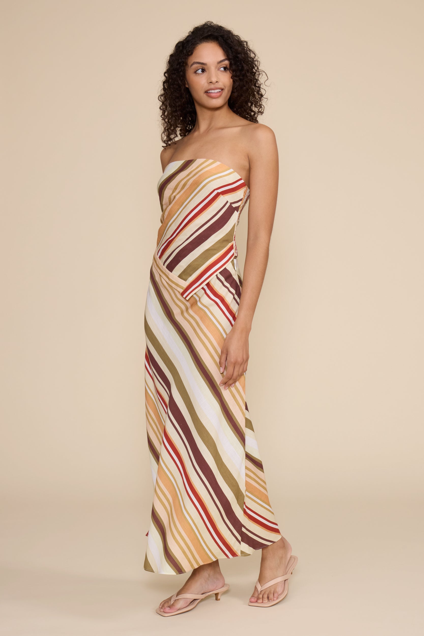 Woman wearing a strapless, long, multicolored striped dress against a beige background