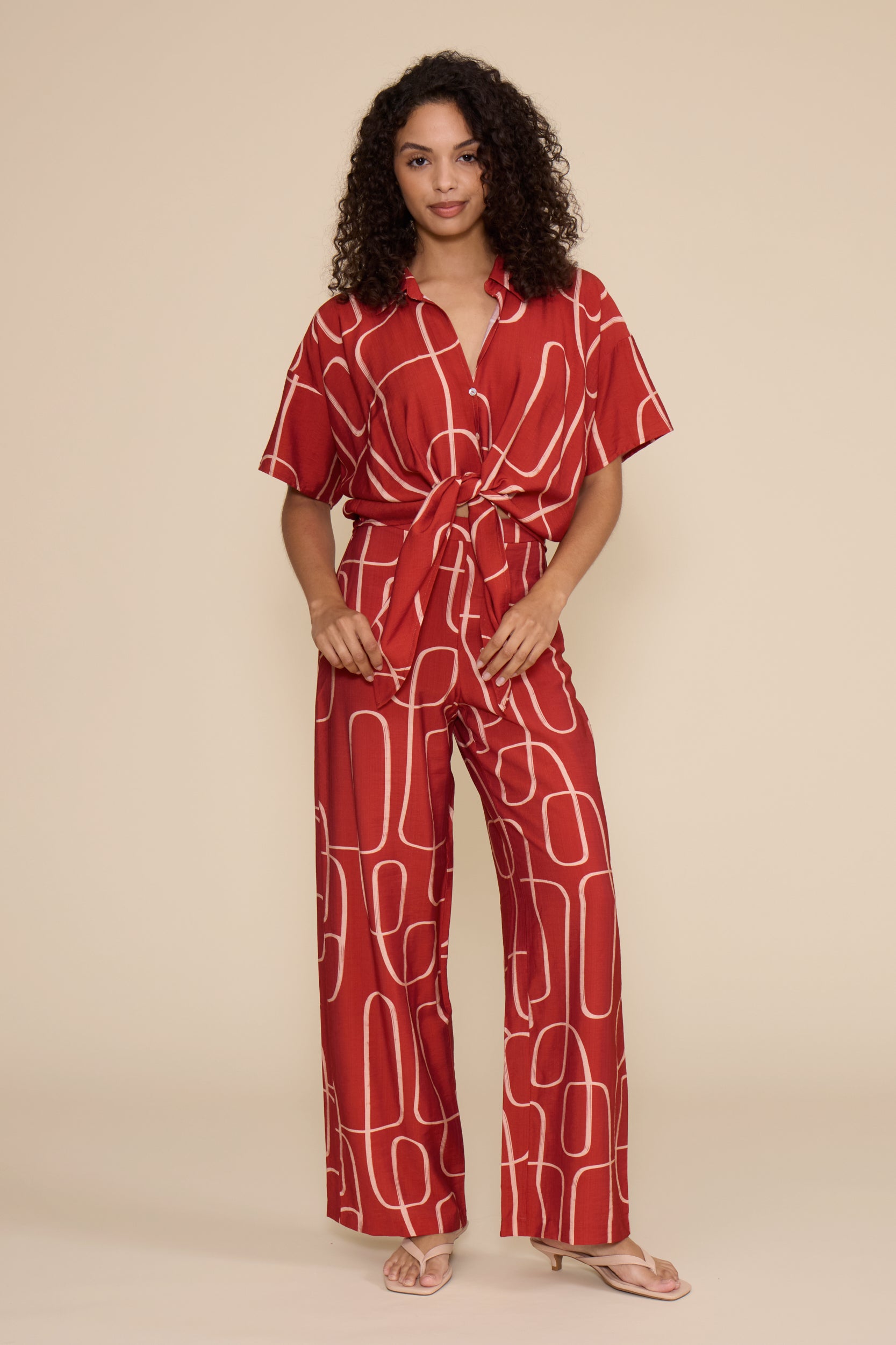 A woman is shown from the side wearing a red short-sleeve wrap dress with a white abstract line pattern, set against a plain beige background.
