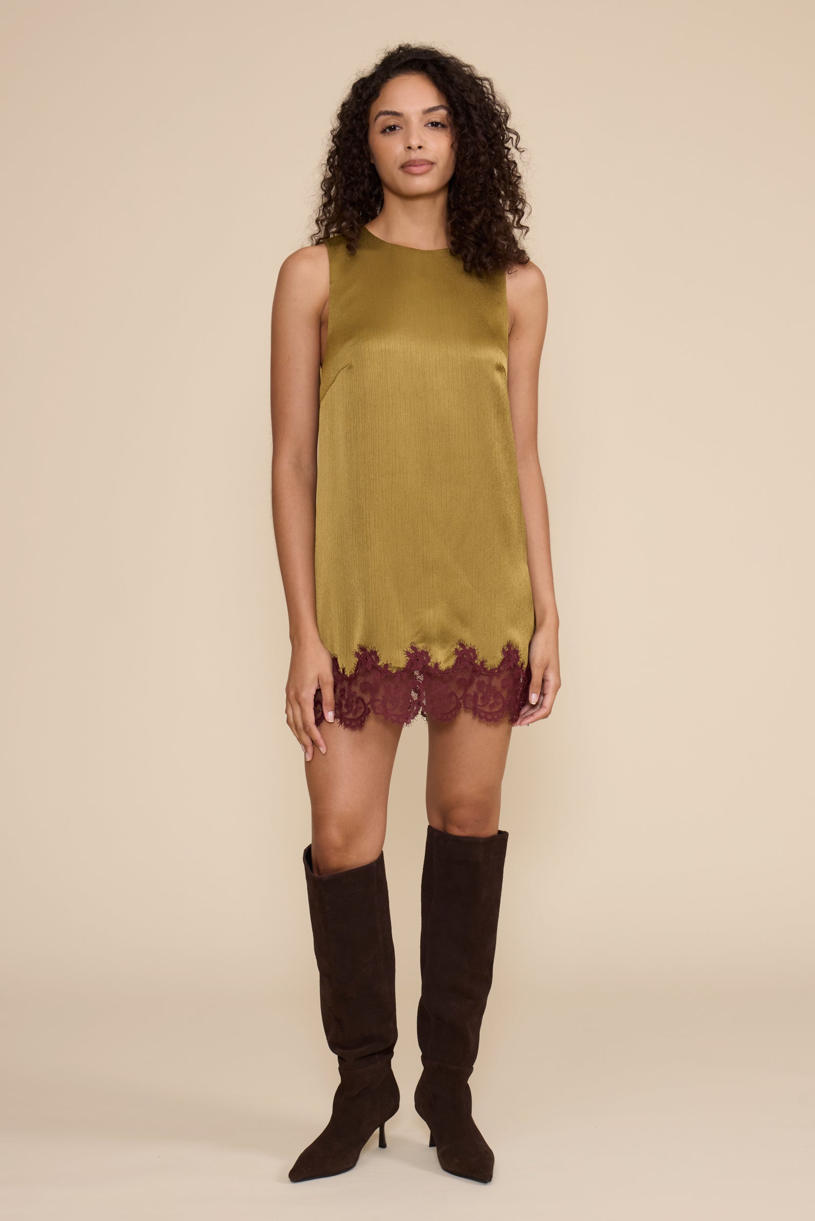 Woman wearing a green dress with lace trim and black knee-high boots on a beige background